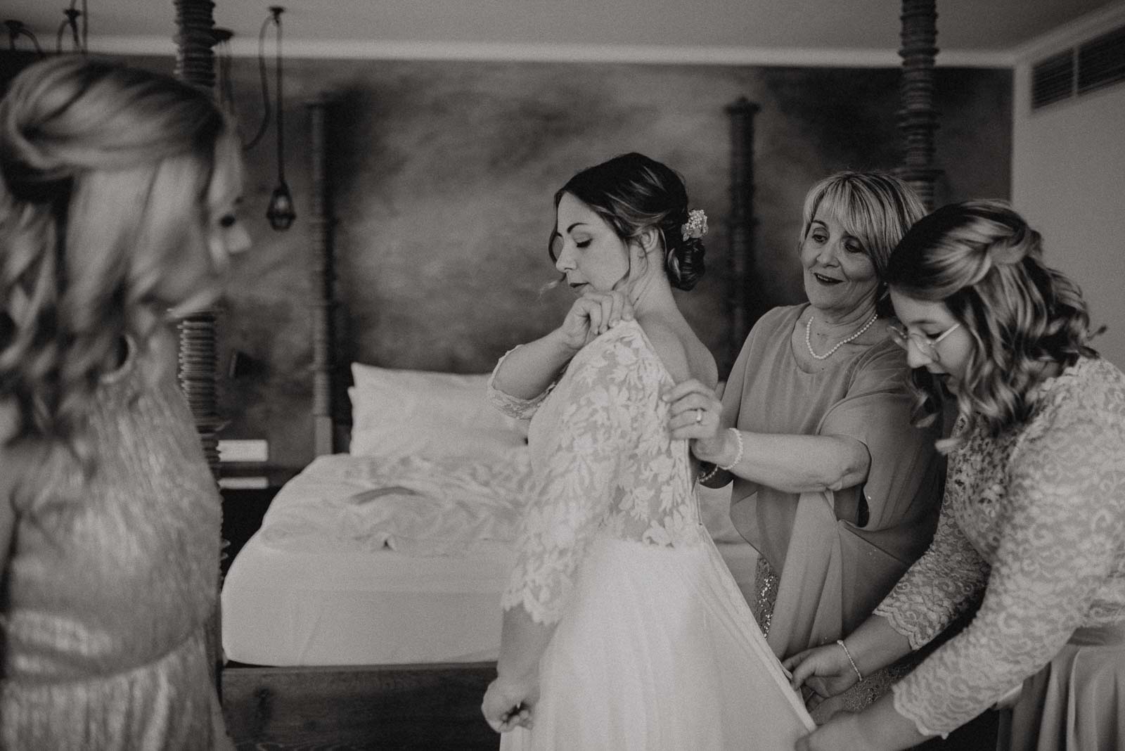 Mutter und Trauzeigin helfen der Braut ins Kleid