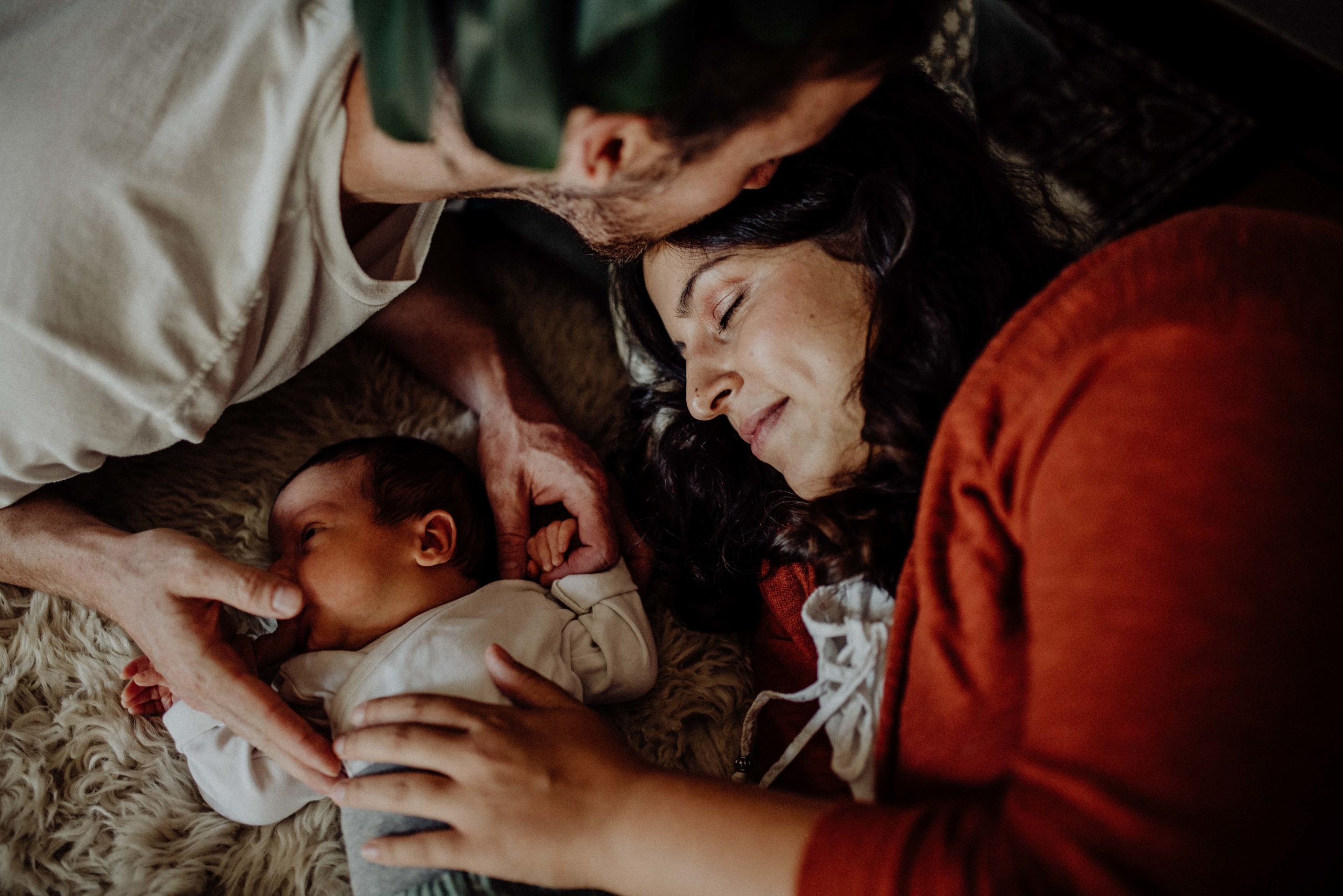 Familie liegt mit Neugeborenem Baby auf Schaffell im Wohnzimmer